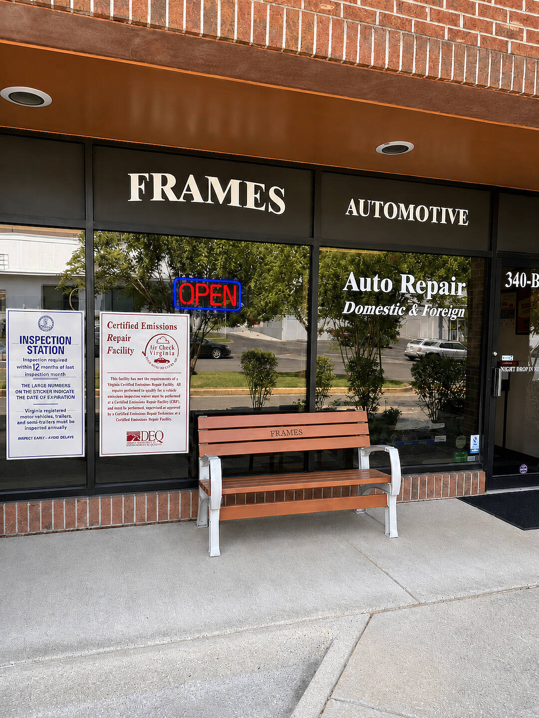 The shop front from the sidewalk, with a bench marked Frames outside the window and the OPEN sign lit